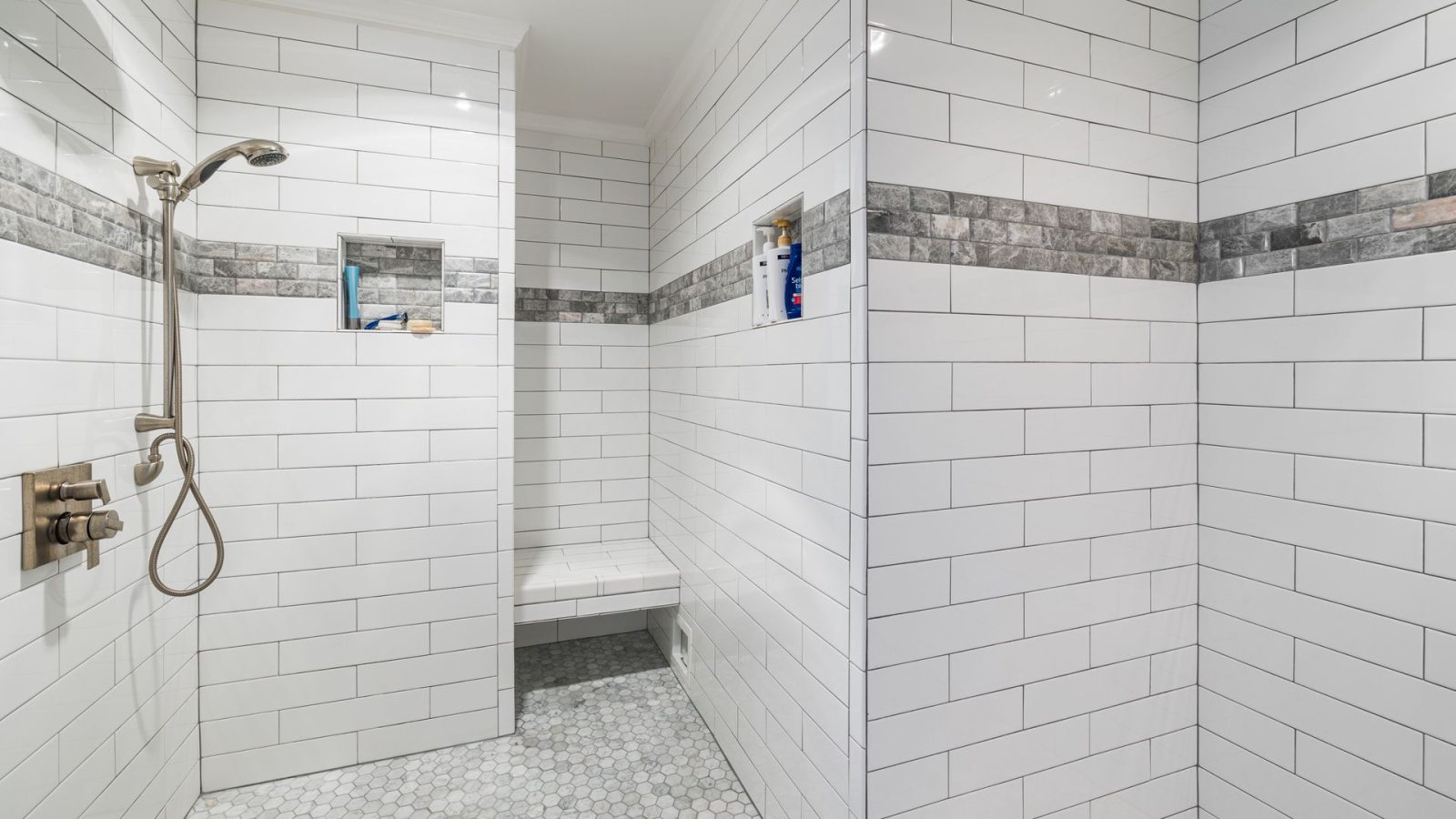Bodengleiche Dusche ohne Duschwanne mit rutschhemmenden Mosaikfliesen am Boden, Sitzbank und Handbrause