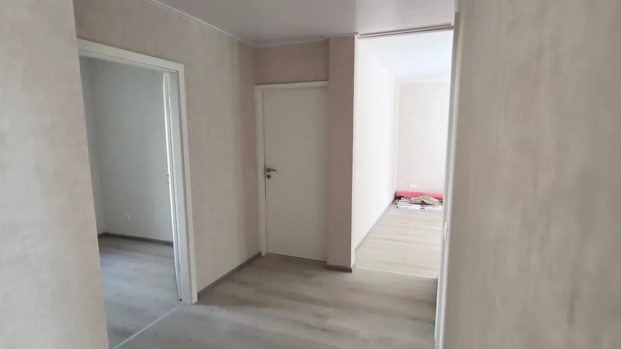 Flur einer renovierten Wohnung mit neuem Vinylboden in Eichenoptik, weißen Innentüren mit Zargen und neu tapezierten Wänden