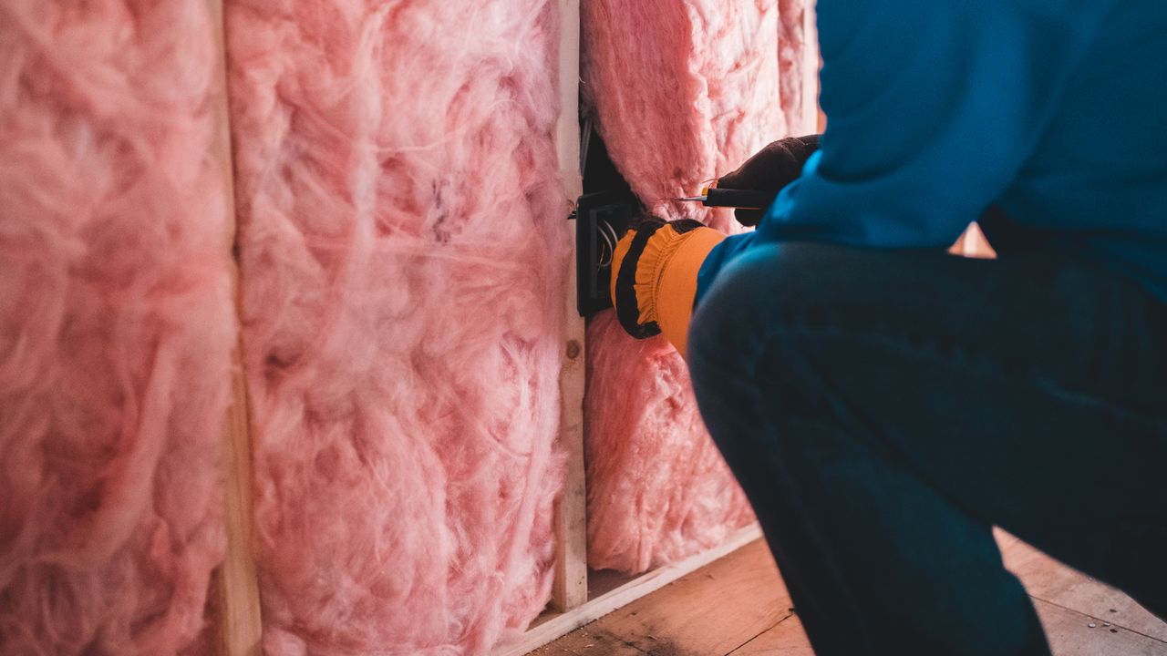Handwerker mit Handschuhen legt Mineralwolle lückenlos in die Gefache einer Unterkonstruktion