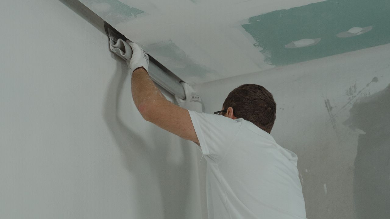 Trockenbauer richtet am Übergang von Decke und Wand ein Profil mit der Wasserwaage aus