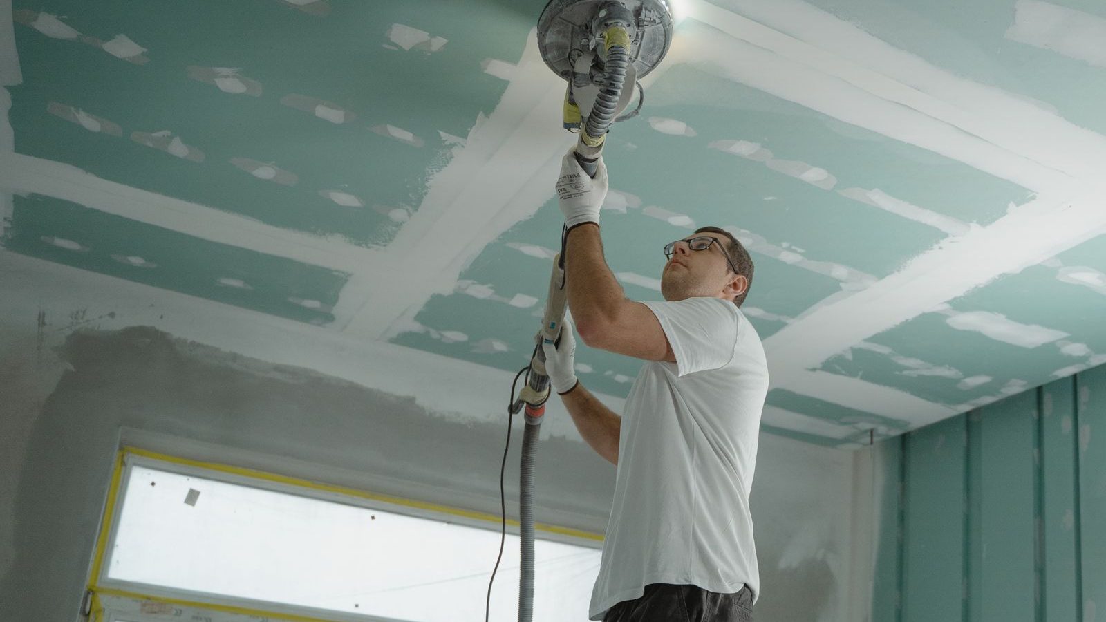 Neue Decke aus Gipskartonplatten wird nach dem Verspachteln mit einem Langhalsschleifer geschliffen