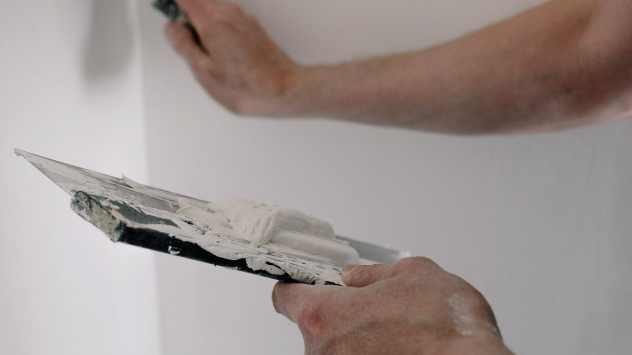 Hände mit Spachtel und Glättkelle tragen Spachtelmasse auf eine Wand auf