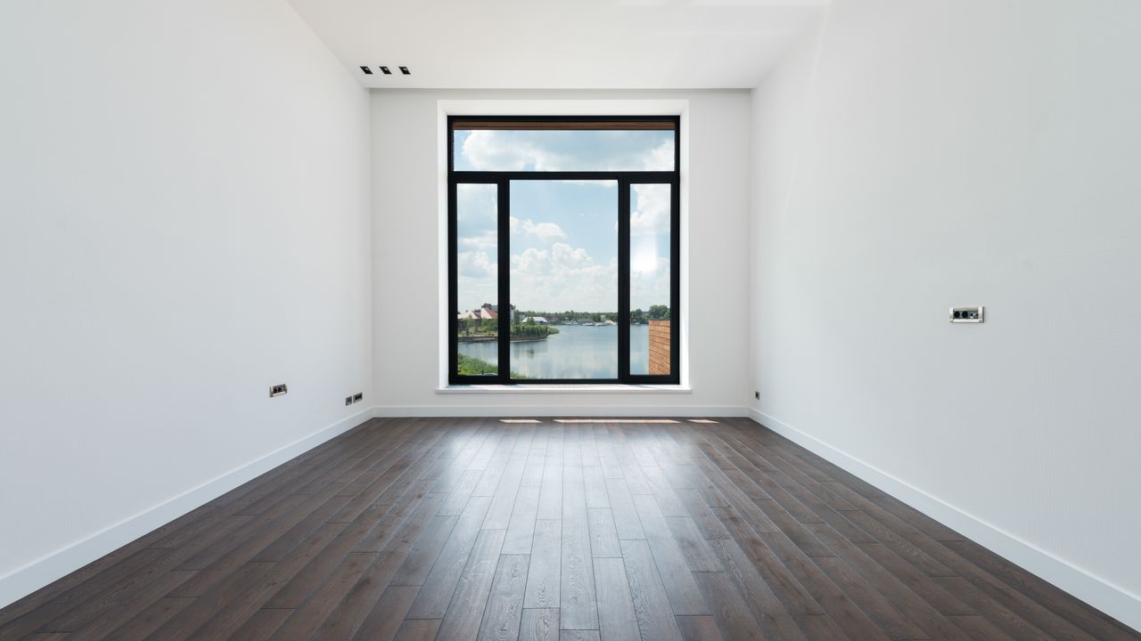Leerer Raum mit dunklem Boden in Holzoptik, weißen Wänden und Sockelleisten